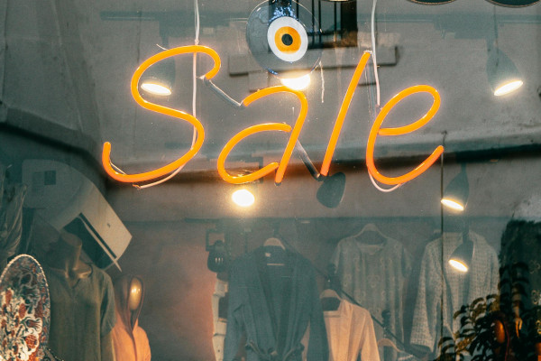 Schaufenster eines Kleidungsgeschäfts, in dem mit einer Leutschrift in orange "Sale" steht.